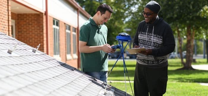 Two students are using a solar pathfinder and a sun eye on a mock roof.