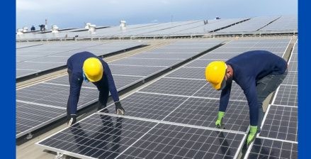 Two people working on solar panels in yellow hard hats.