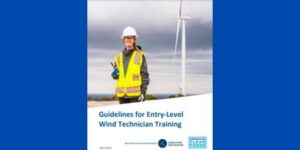 Wind Training Technician in yellow vest and hard hat. Wind Turbine in background. Guidelines for Entry-level Wind Technician Training