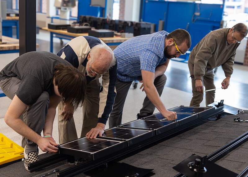 Students inspecting electrical equipment bonding and clamps to solar modules.